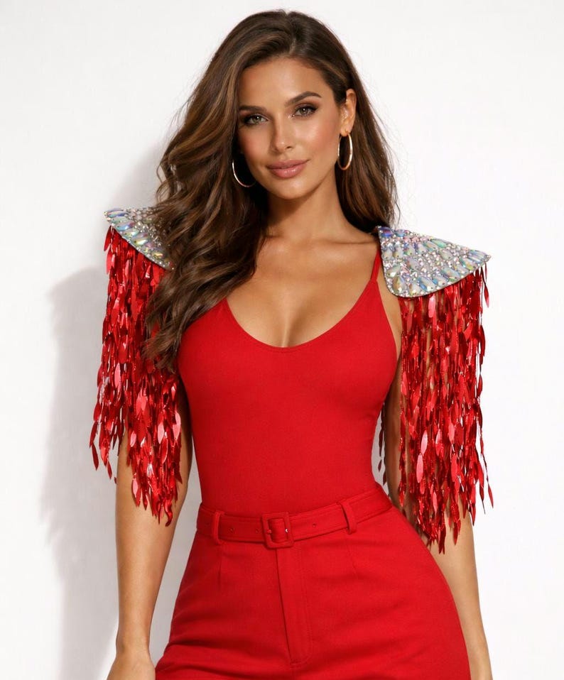 May include: A bright red sleeveless bodysuit paired with matching high-waisted trousers featuring a belt. The garment includes detachable shoulder epaulets adorned with iridescent crystals and long, dangling red sequin fringe accents.