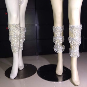 Puede incluir: Dos pares de brazaletes de pierna plateados con un dise&ntilde;o decorativo de diamantes de imitaci&oacute;n. Los brazaletes est&aacute;n en maniqu&iacute;es con piernas blancas.