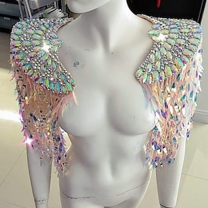 May include: A pair of iridescent shoulder epaulets featuring large, teardrop-shaped crystals and smaller round rhinestones. The shoulder pieces are adorned with long, dangling, light-reflecting sequins that create a shimmering, multi-colored effect.