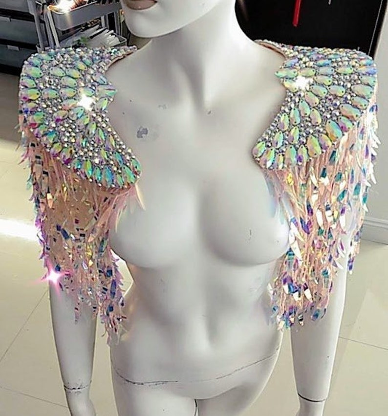 May include: A pair of iridescent shoulder epaulets featuring large, teardrop-shaped crystals and smaller round rhinestones. The shoulder pieces are adorned with long, dangling, light-reflecting sequins that create a shimmering, multi-colored effect.