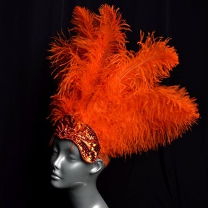 May include: A bright orange feather headdress with a sequined headband. The headband is decorated with orange and gold sequins.