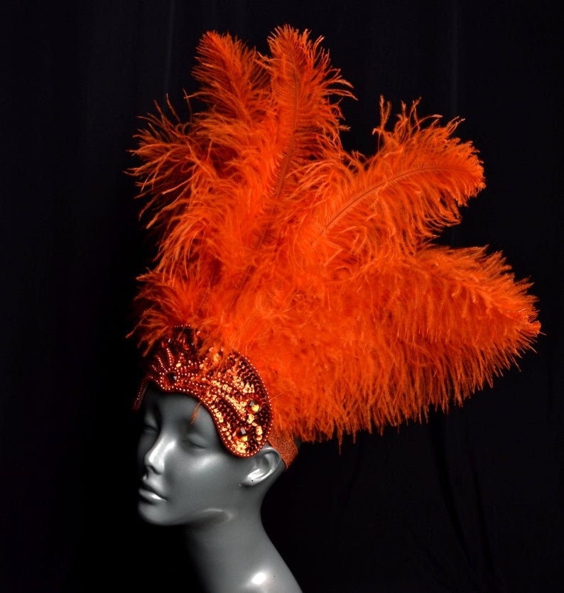May include: A bright orange feather headdress with a sequined headband. The headband is decorated with orange and gold sequins.