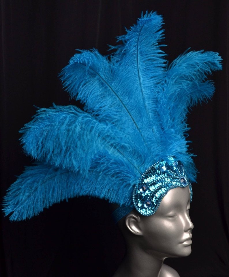 May include: A turquoise feather headdress with a turquoise sequined headband. The headband is decorated with rhinestones.