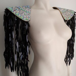 May include: A pair of shoulder epaulets featuring iridescent, multi-faceted crystals on the top panels. Long, dangling black sequin fringe hangs from the edges of each shoulder piece, creating a layered, textured effect across the upper arms.