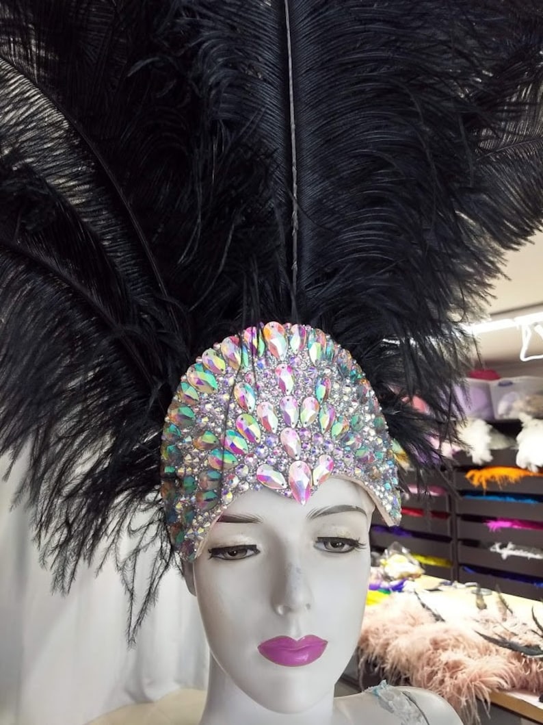 May include: A black feather headdress with iridescent rhinestones. The headdress is worn on a mannequin's head.