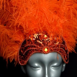 May include: Orange feather headdress with a sequined headband. The headband is decorated with orange and gold sequins and beads.