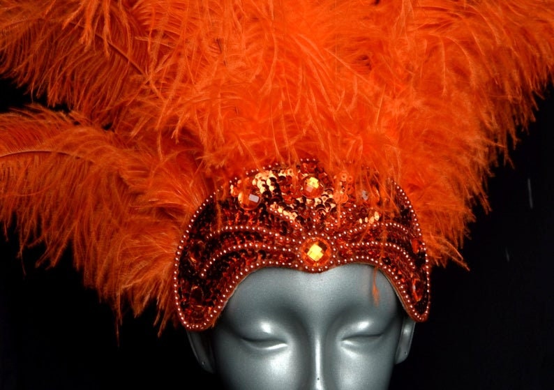 May include: Orange feather headdress with a sequined headband. The headband is decorated with orange and gold sequins and beads.
