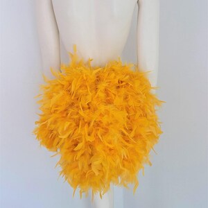 Puede incluir: Una falda de plumas de color amarillo brillante. La falda est&aacute; hecha de plumas esponjosas y es muy voluminosa.