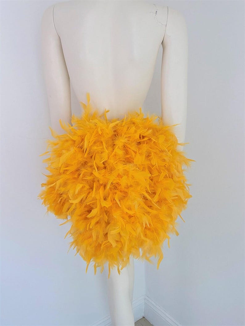 Puede incluir: Una falda de plumas de color amarillo brillante. La falda est&aacute; hecha de plumas esponjosas y es muy voluminosa.