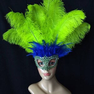 Pode incluir: Uma m&aacute;scara de carnaval verde e azul com strass e penas. A m&aacute;scara est&aacute; em uma cabe&ccedil;a de manequim.