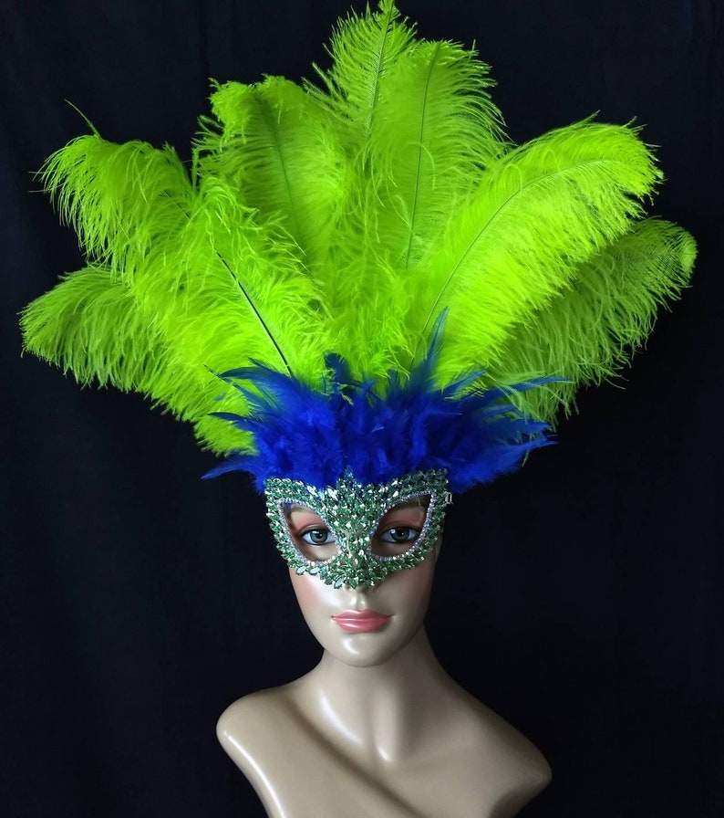 Pode incluir: Uma m&aacute;scara de carnaval verde e azul com strass e penas. A m&aacute;scara est&aacute; em uma cabe&ccedil;a de manequim.