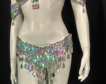 Pode incluir: Um conjunto deslumbrante de traje de dança do ventre, incluindo um sutiã, punhos e um cinto. Cada peça é adornada com strass iridescentes e enfeites pendurados. O sutiã e o cinto apresentam um design em cascata, criando um visual glamouroso.