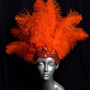 May include: A bright orange feather headdress with a beaded headband. The headband is decorated with rhinestones and sequins.