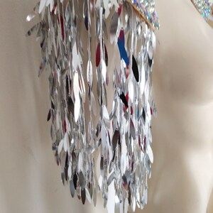 May include: A pair of shoulder epaulets featuring a top layer of iridescent, multi-colored sequins and a cascading fringe of long, reflective silver leaf-shaped metallic pieces that hang down to create a shimmering, high-contrast visual effect.
