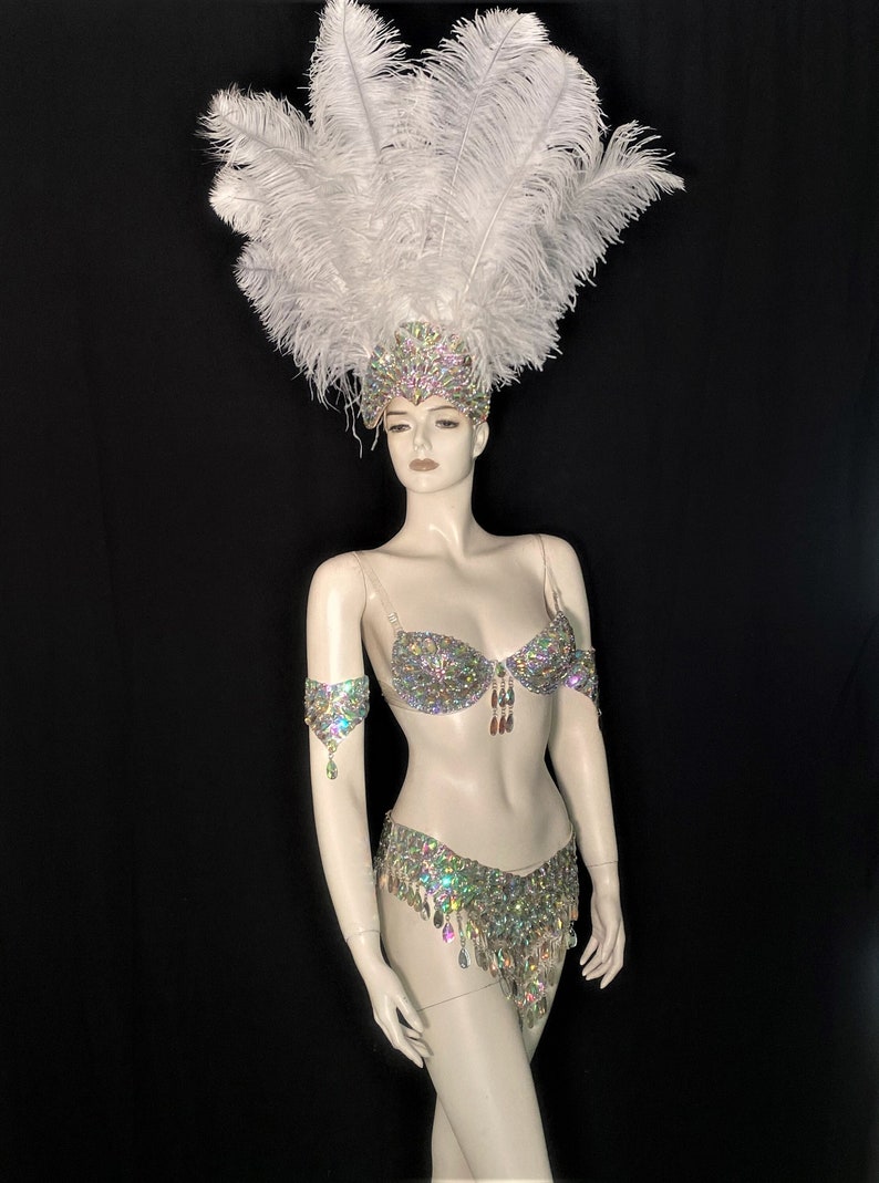 May include: A white feather headdress with a silver and iridescent crystal bra and matching skirt. The costume is worn by a mannequin.