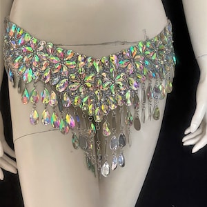 May include: A silver-toned belly chain with iridescent crystal embellishments. The chain features a row of flower-shaped crystals and a fringe of teardrop-shaped crystals.