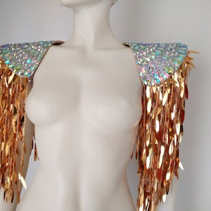 May include: A pair of gold shoulder pieces with iridescent crystal embellishments and gold fringe.