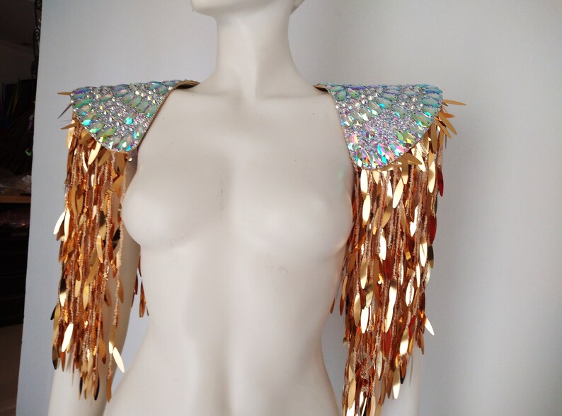 May include: A pair of gold shoulder pieces with iridescent crystal embellishments and gold fringe.