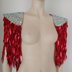 May include: A pair of shoulder epaulets featuring iridescent, multi-faceted crystals arranged on the top panels, with long, dangling, metallic red sequin fringe extending downward from the edges to create a layered, reflective appearance.