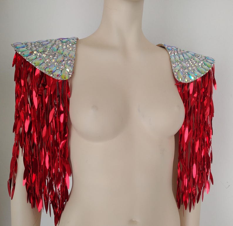 May include: A pair of shoulder epaulets featuring iridescent, multi-faceted crystals arranged on the top panels, with long, dangling, metallic red sequin fringe extending downward from the edges to create a layered, reflective appearance.