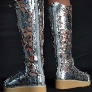 May include: Silver leather boots with cutouts and a zipper up the back. The boots have a thick platform sole.