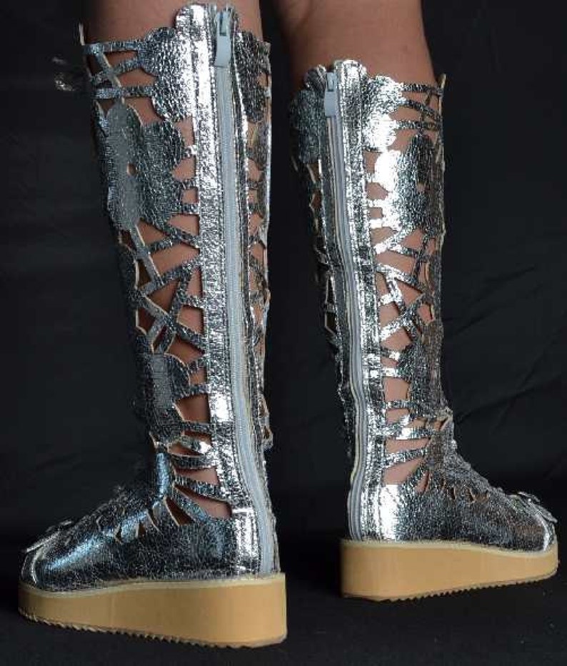May include: Silver leather boots with cutouts and a zipper up the back. The boots have a thick platform sole.