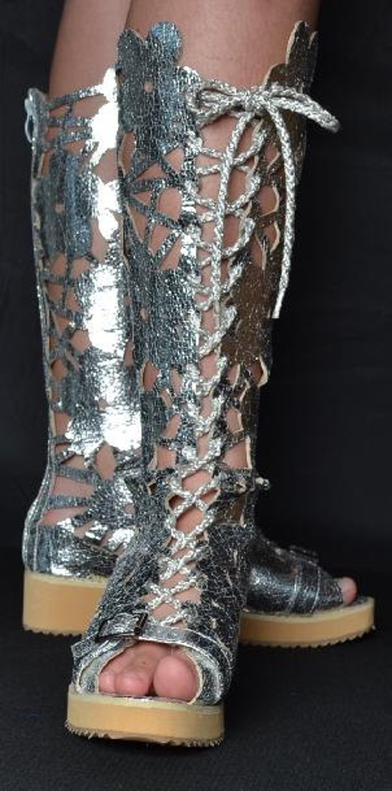 May include: Silver leather lace-up boots with a cut-out design. The boots have a thick platform sole and a closed toe.
