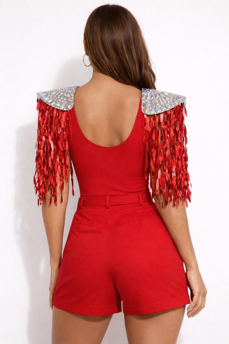 May include: A bright red bodysuit featuring shoulder epaulets adorned with iridescent crystals and long, dangling red sequin fringe. The garment includes a matching red high-waisted short with a thin belt, creating a cohesive monochromatic look.