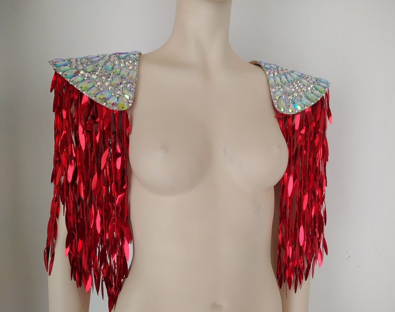 May include: A pair of red sequined shoulder pieces with a silver iridescent base. The shoulder pieces are made of a fabric with a fringe design.