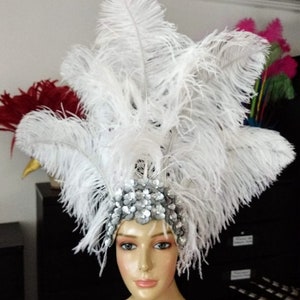 May include: A white feather headdress with a silver sequined band. The headdress is worn on a mannequin's head.