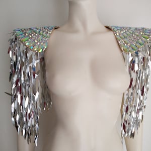 May include: A pair of shoulder epaulets featuring iridescent, multi-colored oval crystals arranged in a dense pattern on the top, with long, dangling silver metallic fringe strips hanging down from the edges to create a reflective effect.