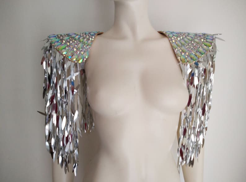 May include: A pair of shoulder epaulets featuring iridescent, multi-colored oval crystals arranged in a dense pattern on the top, with long, dangling silver metallic fringe strips hanging down from the edges to create a reflective effect.