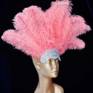 May include: A pink feather headdress with a white beaded headband. The headdress is made of a large cluster of pink feathers.