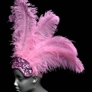 May include: Pink feather headband with a purple sequined eye mask. The headband is worn on a mannequin's head.
