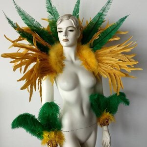 May include: A yellow and green feather costume with gold accents. The costume includes a shoulder piece and two arm cuffs.