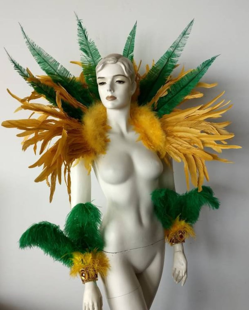 May include: A yellow and green feather costume with gold accents. The costume includes a shoulder piece and two arm cuffs.