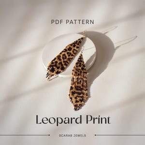 Könnte beinhalten: PDF-Muster für ein Paar lange, geperlte Ohrringe mit Leopardenmuster. Die Ohrringe hängen an einer weißen runden Oberfläche. Der Text "Leopard Print" und "SCARAB JEWELS" ist unter den Ohrringen zu sehen.