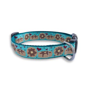 May include: A turquoise blue dog collar with a pattern of brown pancakes and red hearts. The collar has a silver buckle and a black D-ring.
