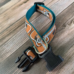 May include: A teal and brown dog collar with a guitar print. The collar has a black plastic buckle.