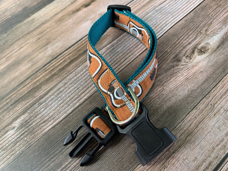 May include: A teal and brown dog collar with a guitar print. The collar has a black plastic buckle.