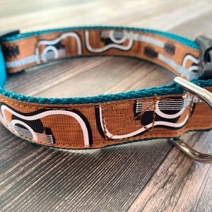 May include: Teal dog collar with a brown, white, and black geometric pattern. The collar has a silver metal D-ring.