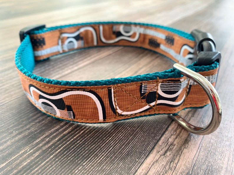 May include: Teal dog collar with a brown, white, and black geometric pattern. The collar has a silver metal D-ring.