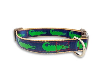 May include: A blue dog collar with a tan trim and a green alligator pattern. The collar has a silver D-ring and a brown plastic buckle.