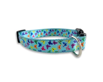 May include: A light blue dog collar with a colorful butterfly pattern. The collar has a black plastic buckle and a silver metal D-ring.