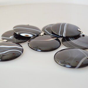 May include: A group of seven black and white agate pendants with silver bail loops. The pendants are round and have a polished finish.