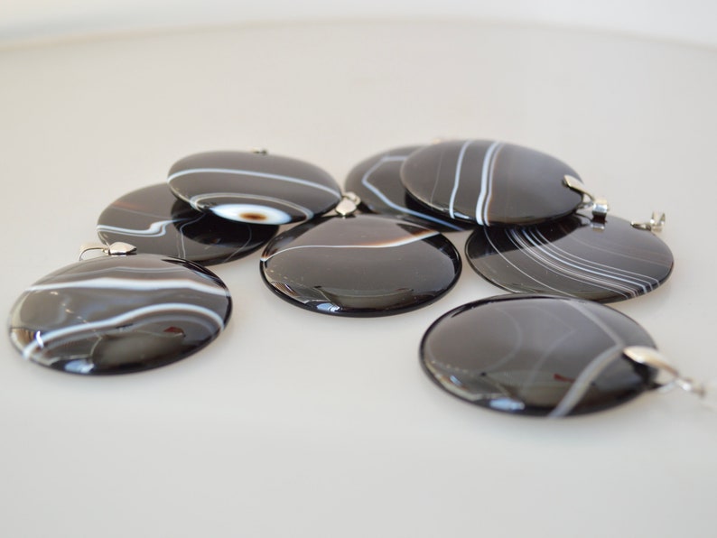 May include: A group of seven black and white agate pendants with silver bail loops. The pendants are round and have a polished finish.