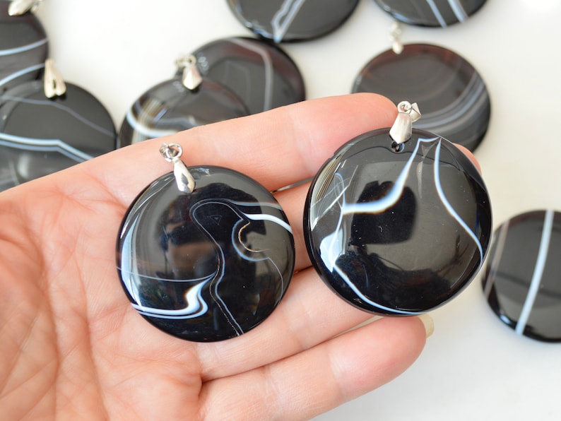 May include: Two black and white agate pendants with silver bail. The pendants are round and have a swirling pattern of white lines on a black background.