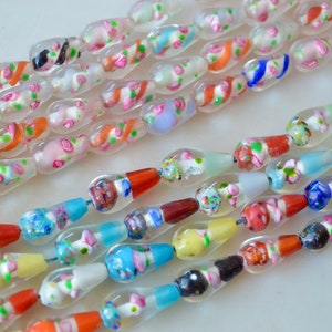 May include: A strand of colorful glass beads with a variety of patterns and designs. The beads are clear and translucent, with some having a white or pink base. The beads are strung on a wire and are arranged in a random order.