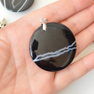 May include: Black and white agate pendant with a silver bail. The pendant is round and has a smooth, polished surface. The agate has a natural pattern of white lines on a black background.