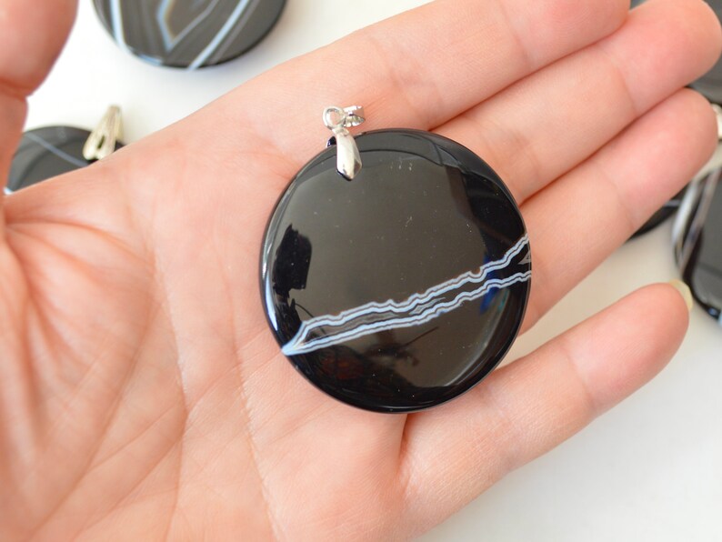 May include: Black and white agate pendant with a silver bail. The pendant is round and has a smooth, polished surface. The agate has a natural pattern of white lines on a black background.